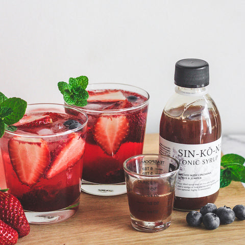 Sinnkonah tonic syrup next to two cocktails with berries and mint