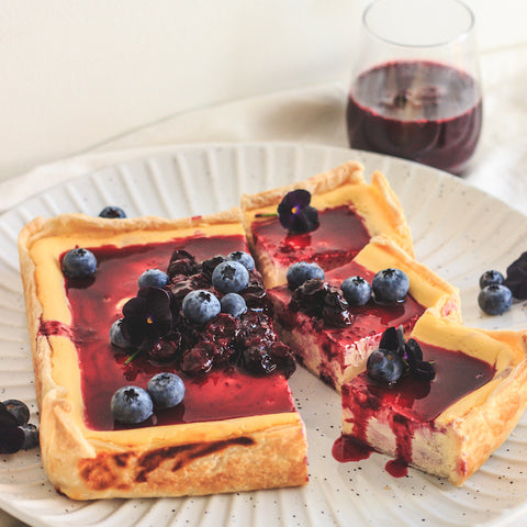 A square cheesecake on white plate with berries on top.