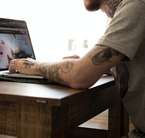 man with short sleeves and tattoos playing on a laptop