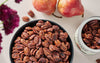 bowl of Fortune Favors candied pecans with fruit and flowers in background