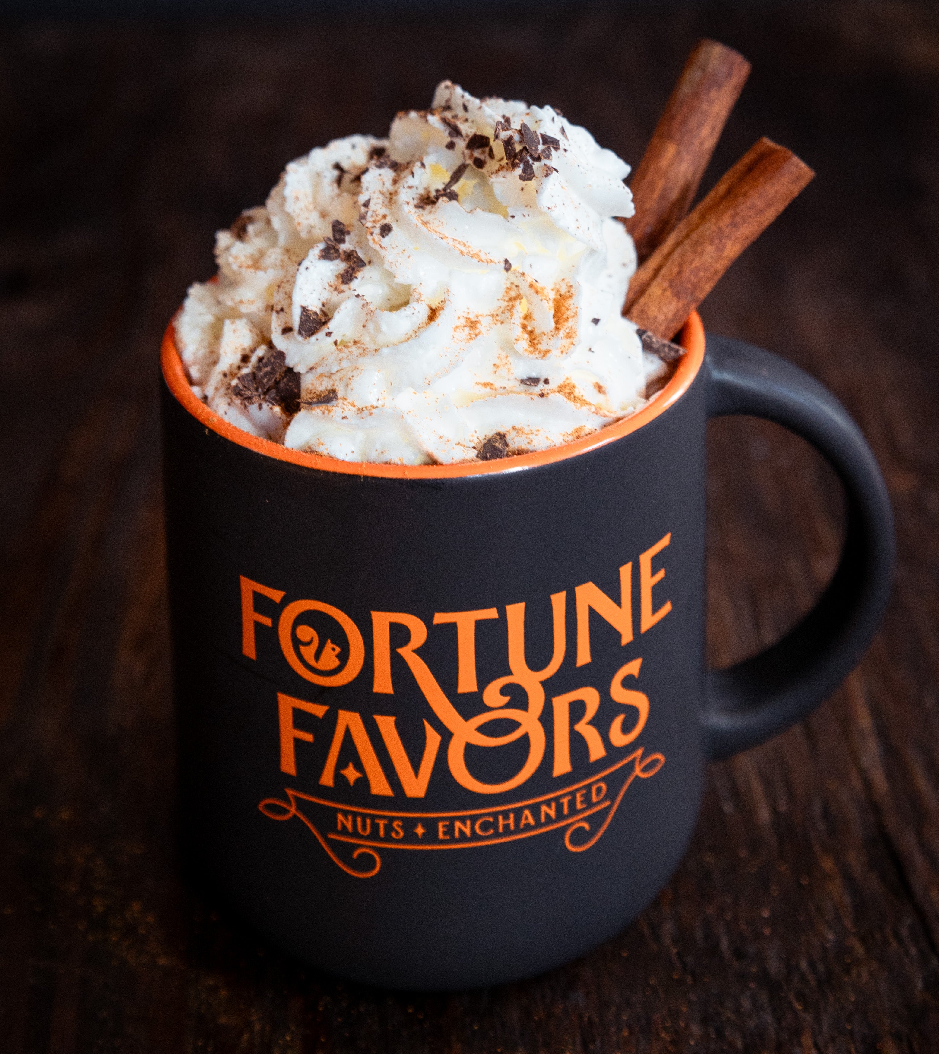 Fortune Favors branded coffee mug with whipped cream and cinnamon sticks garnish.
