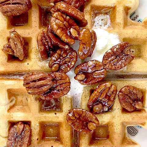 Close-up photo of waffle with pecans, butter, and syrup.