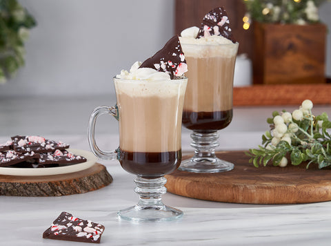 A photograph of two glass mugs with Peet's peppermint bark coffee inside and whipped cream on top, plus a plate of peppermint bark to the side