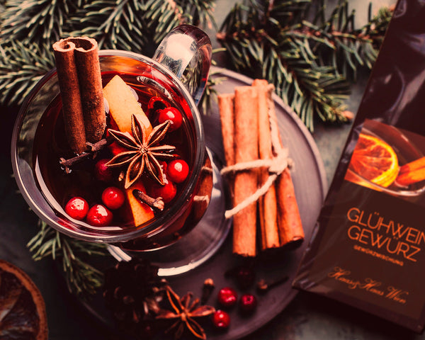 Glühwein im Glas mit Cranberries und Sternanis, Zimtstangen und Orangen.