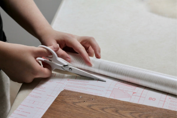 Hands holding white scissors cutting vinyl using backing paper grid as a guide