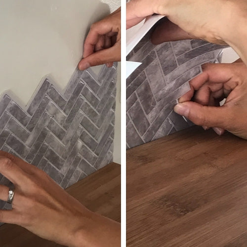 Grey herringbone peel and stick tiles being applied onto white wall above oak benchtop