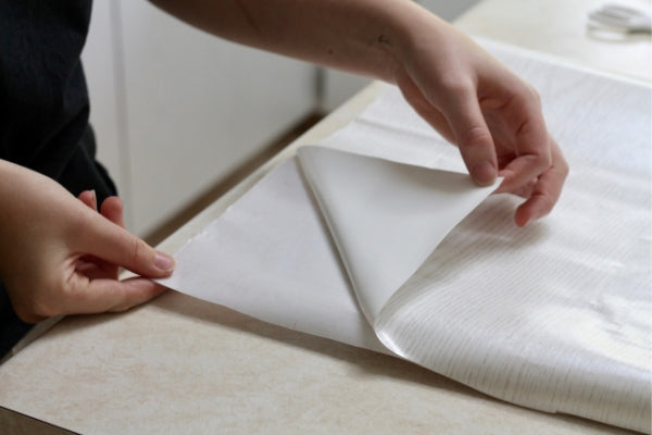 hands folding a corner of sticky back plastic away from backing paper