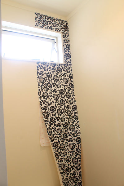 One strip of black and white wallpaper hanging down to the right of window