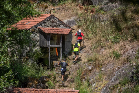 Three trail runners climbing a trail with a forest landscape with an old house.