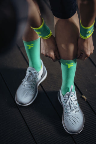 Person pulling up Fyke's light green mid socks wearing wristbands of the same color.