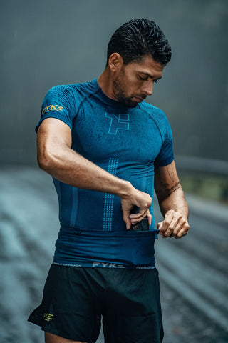 A man wearing a blue Fyke seamless T-shirt putting his cell phone in the blue Fyke Boost Running Belt.