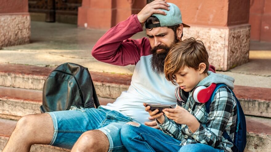 A dad whatching his son playing a casual game on mobile