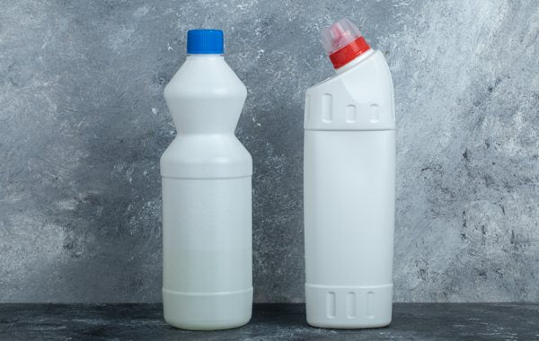 Two bottles of bleach resting on a countertop surface.