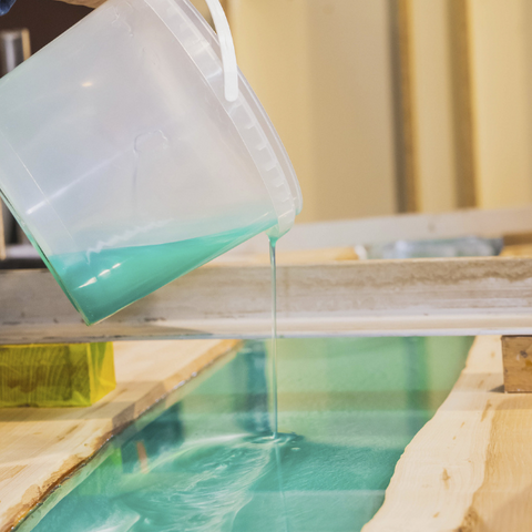 Pigmented epoxy resin being poured into a river table vein from a large round mixing container