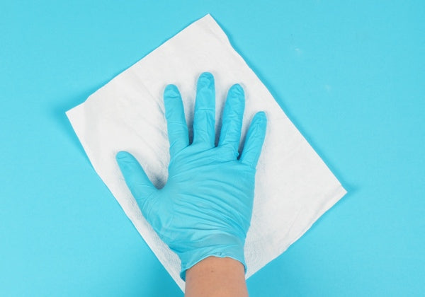 A gloved hand cleaning a surface with a paper towel