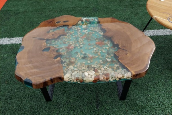 A sea-themed epoxy coffee table made with a live-edge slab of wood, resin tinted with blue dyes, and various sea-themed embedments.