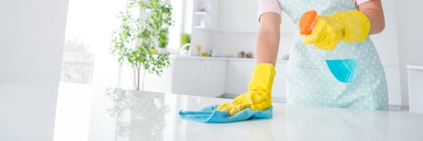 A gloved hand wiping down an epoxy countertop with glass cleaner and a microfiber.