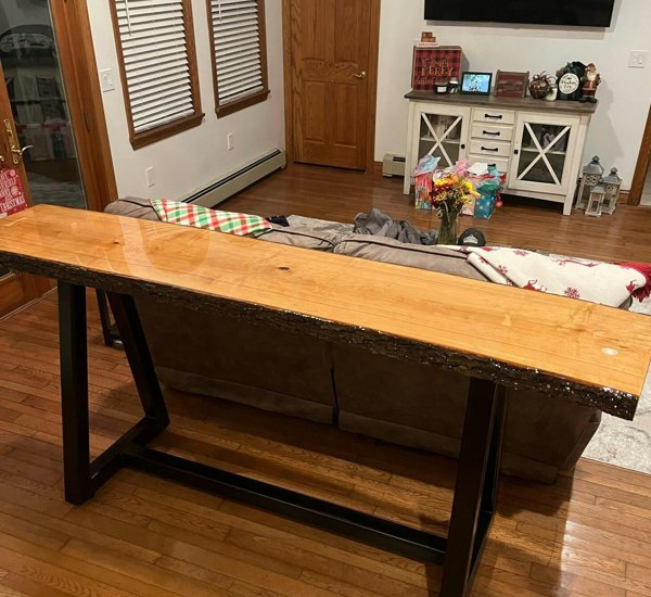 A slim live-edge wooden epoxy resin table standing behind a couch.