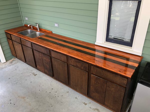 An outdoor wooden epoxy bar top with two parallel epoxy river veins tinted with black epoxy pigments.