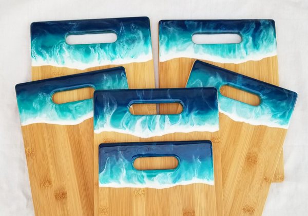 Six different wooden cutting boards with epoxy resin ornamentation around their grips.