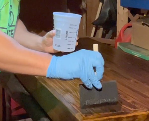 A seal coat batch of epoxy resin being applied to a wooden bar top surface.