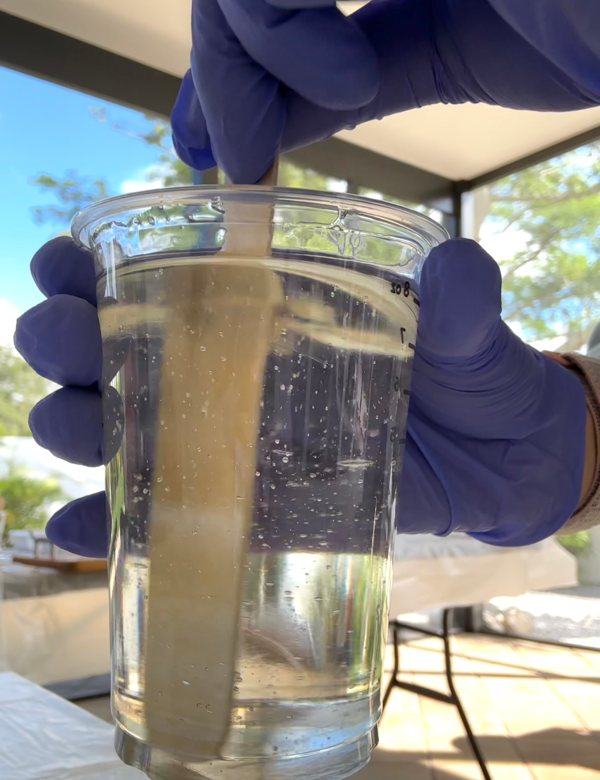 A small batch of epoxy resin being mixed in a clear plastic cup with a wooden stir stick.