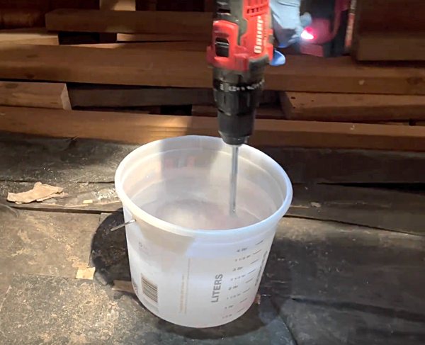 A large flood coat batch of epoxy resin being blended together with a mixing drill bit attached to a power drill.