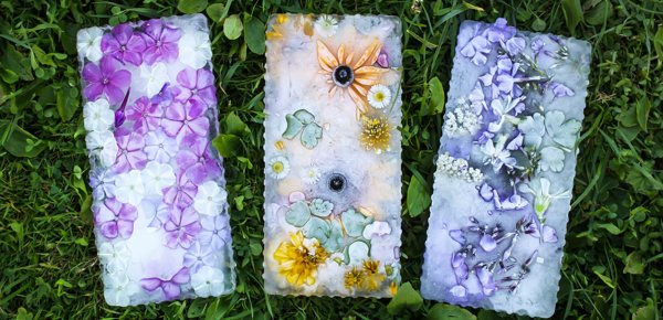 Three beautiful flower-themed resin bookmarks resting on some grass.