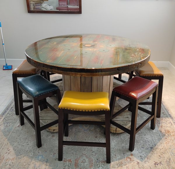 A round wooden epoxy resin table surrounded by colorful stools.