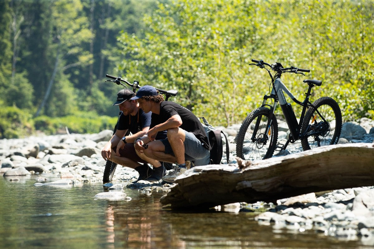 Two mountain bikers with Shred eMTBs parked near river