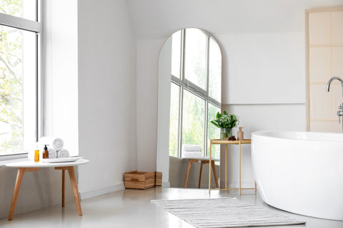 A large frameless free standing arch leaner mirror against the wall in a modern white bathroom