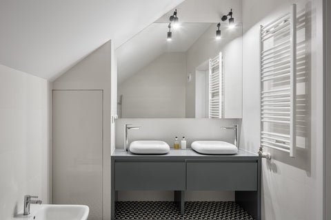 A modest bathroom with his and hers sink and a rectangular mirror above with left corner cut off to fit the arched ceiling.