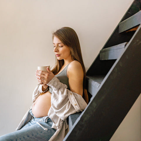 pregnant woman sitting on stairs drinking coffee