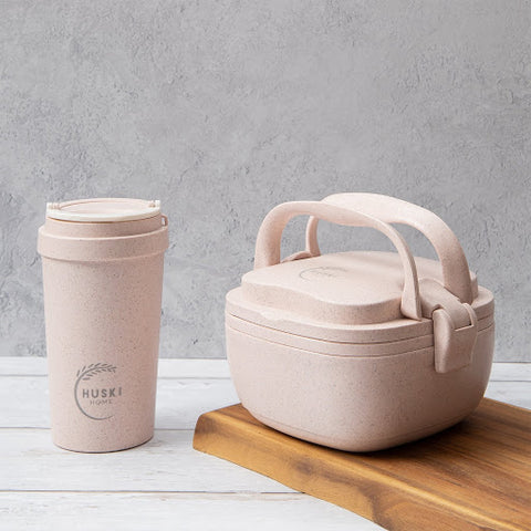 Eco friendly lunchbox and matching takeaway coffee cup in a dusty pink on a wooden chopping board.