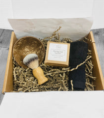 Open gift box with coconut shell bowl, shaving brush, small brown box with soap inside, and a black cotton washcloth