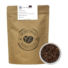 Large paper bag with a bowl of fresh coffee beans to the right of the bag. Text on the bag reads Recent Beans, freshly roasted is better in a circle logo