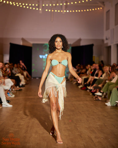 Black woman with curly hair wearing aqua strapless two piece bikini with a ivory fringe cover up skirt