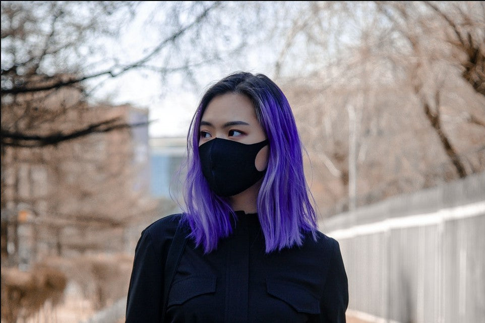 a woman with purple hair wearing a black sweater and a mask