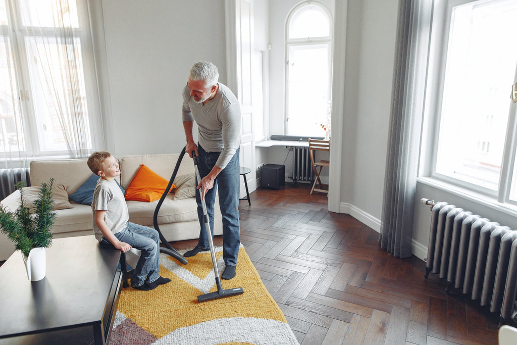 cheerful father talking with son while vacuuming