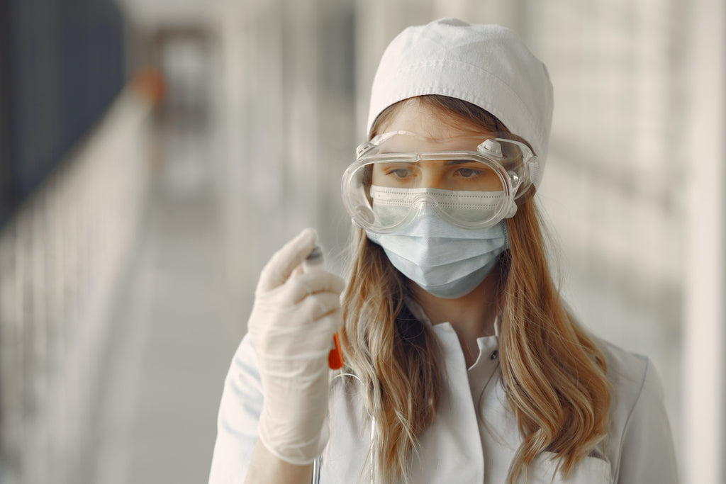 a woman wearing face mask, eye goggles, and white gloves looking at a blood sample