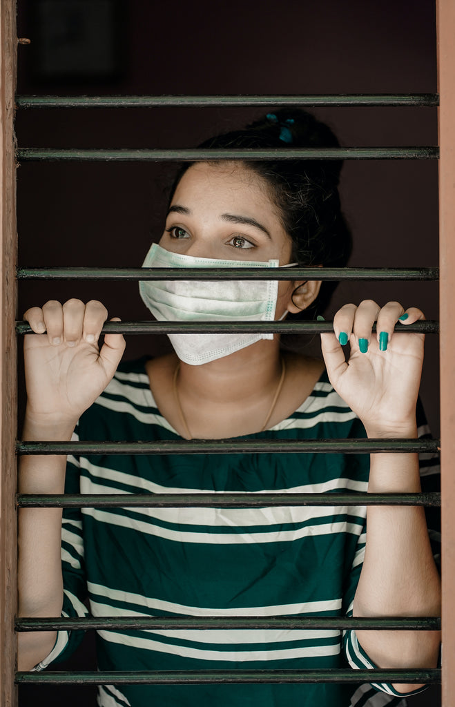 woman in green and white stripes wearing facemask holding on her window bars