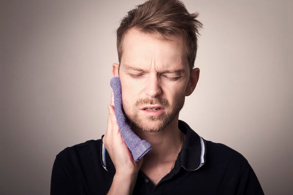 Man holding the side of his face in pain with towel