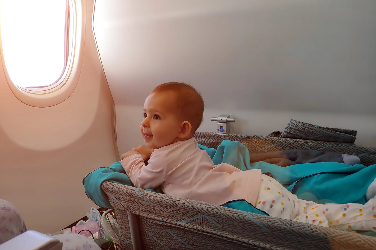 Baby lying on her stomach in a bassinet on an airplane facing the plane’s window