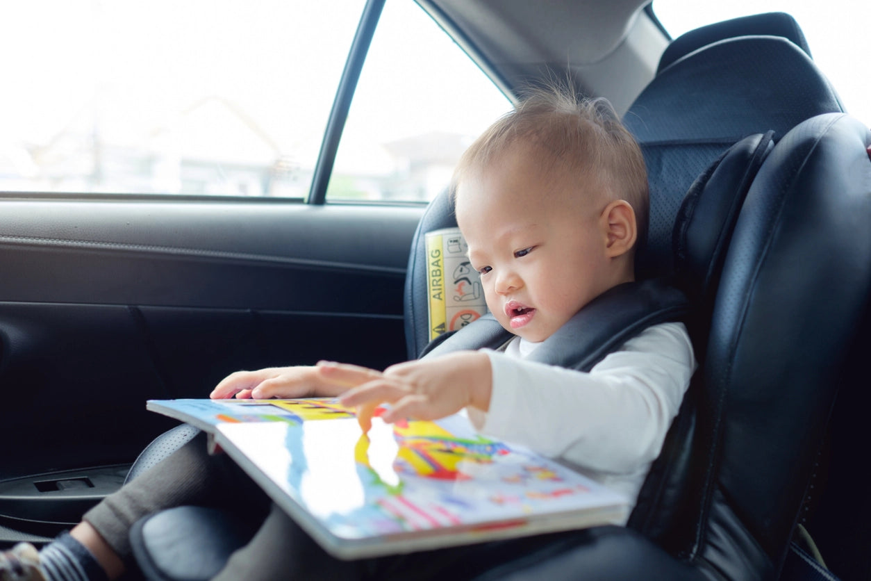 Toddler boy sitting in a car seat reading a book