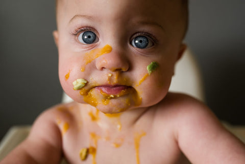 Baby weaning with food all over its face