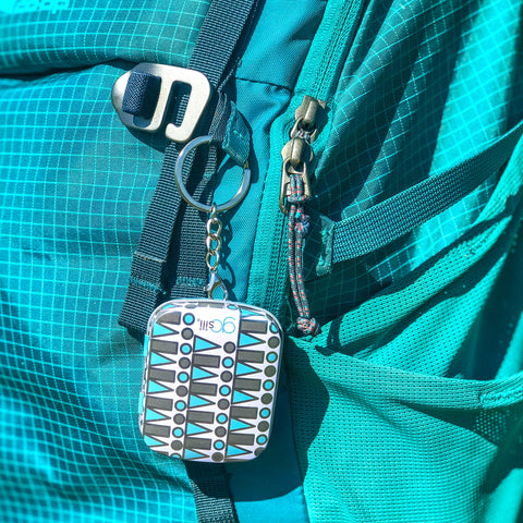 A blue backpack with a keychain attached to it. The keychain has a reusable silicone straw inside a tin. 