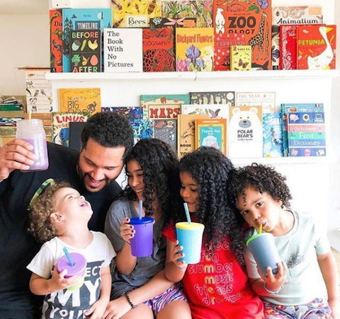 Dad, mom, and three kids sitting on a sofa holding reusable silicone cups and smiling while looking at each other.