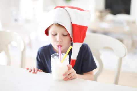 Kid sitting at table with a christmas hat on sipping from a glass using a reusable sustainable silicone straw