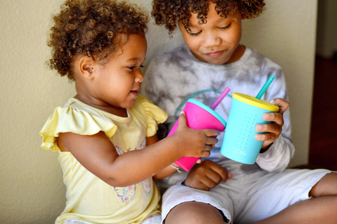 Two kids holding their reusable silicone cups with straw