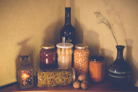A set of glass jars sit in a pantry filled with food preserves like corn, green beans, chickpeas, and more. 